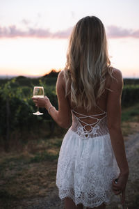 Rear view of young woman holding wineglass while standing on land