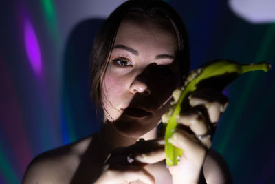 Close-up portrait of young woman holding banana in darkroom