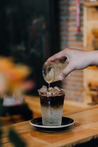 Cropped hand pouring drink in glass on wooden table