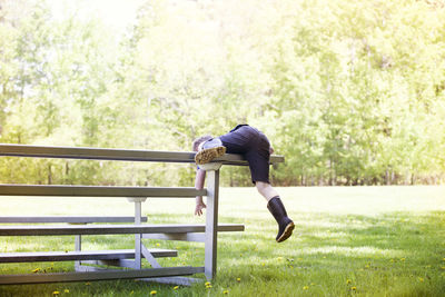 Playful boy climbing on bench at park