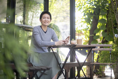 Smiling woman looking away while sitting on table against trees