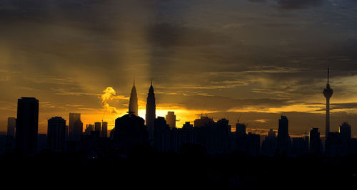 Silhouette petronas towers amidst buildings in city during sunrise