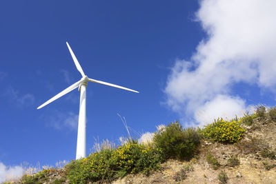 Low angle view of windmill on field against blue sky