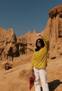 Woman shielding eyes while standing against rock formations