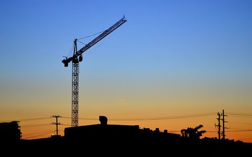 Low angle view of silhouette crane against sky during sunset