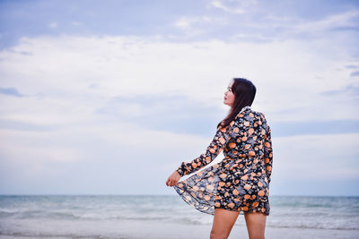 Woman wearing dress standing at beach against sky