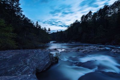 Scenic view of river stream amidst trees against sky