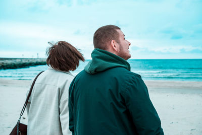 Rear view of friends at beach against sky