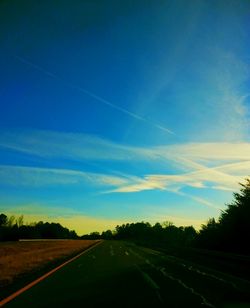 Road passing through field against cloudy sky