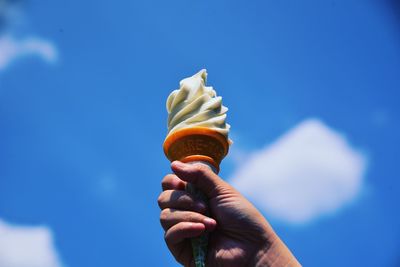 Hand holding ice cream cone against blue sky
