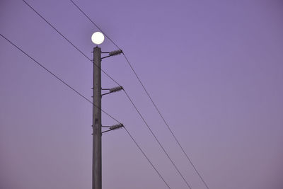 Low angle view of electricity pylon against clear sky at dusk
