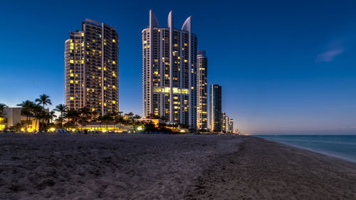 Illuminated city by sea against blue sky at night