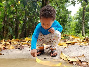 Boy holding leaf in lake at forest