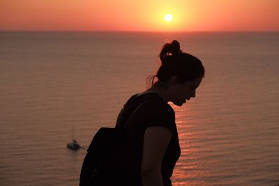 Silhouette young woman standing by sea against sky during sunset