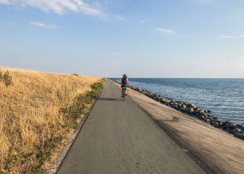 Rear view of woman riding bicycle on road by sea