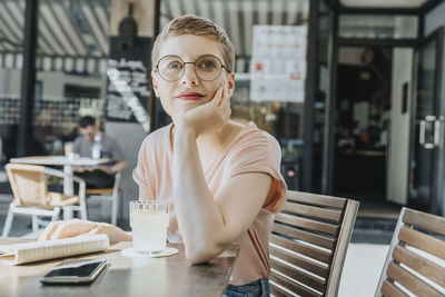 Woman sitting with hand on chin in sidewalk cafe during sunny day