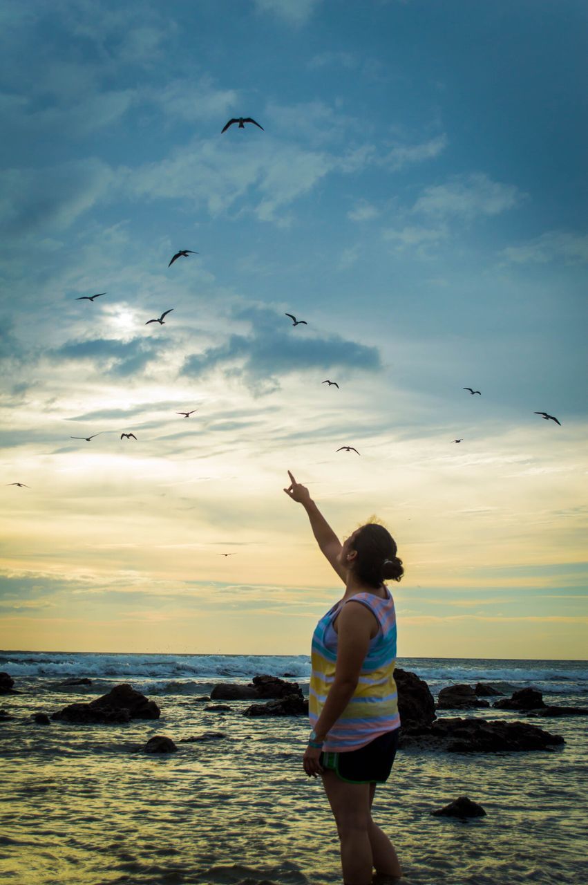 flying, sea, one person, sky, beach, cloud - sky, water, real people, bird, horizon over water, children only, standing, leisure activity, nature, animal themes, childhood, day, outdoors, flock of birds, wave, beauty in nature, people, adult