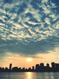 Silhouette buildings by sea against sky during sunset