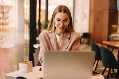 Portrait of a business woman student wearing headphones smiling drinking coffee working online