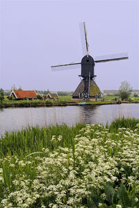 Traditional windmill by river against sky