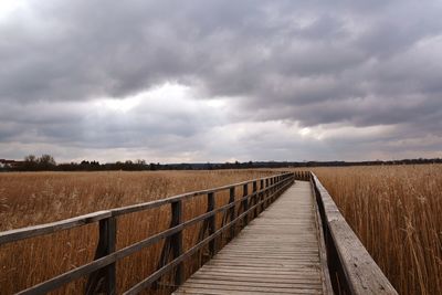 Road passing through field against cloudy sky