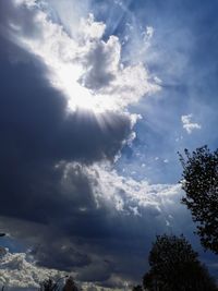 Low angle view of sunlight streaming through clouds