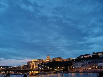 Illuminated bridge over river against buildings at dusk