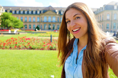 Portrait of smiling young woman standing against buildings