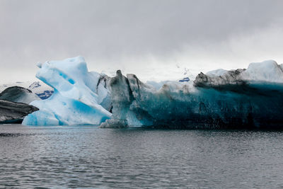 Scenic view of sea by glacier against cloudy sky