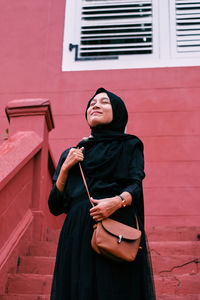 Young woman looking away while standing against wall