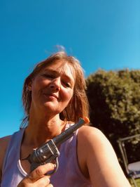 Portrait of woman looking at camera against blue sky