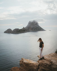 Man standing on rock by sea against sky