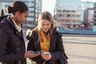 Friends looking away while standing on mobile phone