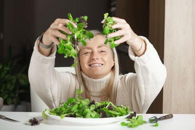 Smiling mature woman holds a full handful of green lettuce, diet and healthy lifestyle concept