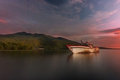 Abandoned boat in sea against mountain during sunset