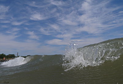 Sea waves splashing on shore against sky