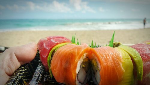 Close-up of hand holding a sushi plate against sea