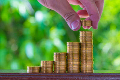 Cropped hand stacking coins on table against plants