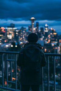 Rear view of man looking at illuminated city buildings