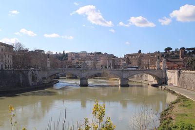 Arch bridge over river in city against sky