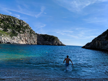 Full length of shirtless man in sea against sky