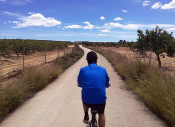 Rear view of man walking on road against sky
