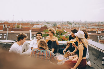 Friends enjoying beer while sitting together on terrace at rooftop party