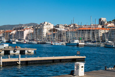 Sailboats moored at harbor in city against clear blue sky