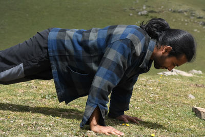 Side view of a good looking indian young man with ponytail hair style doing push ups in the mountain