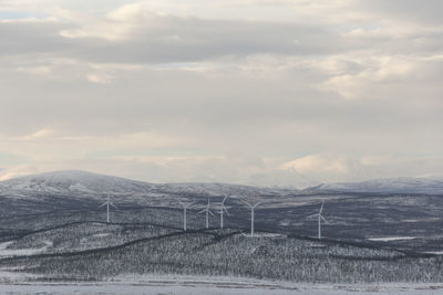 Scenic view of snowy landscape with wind turbines against sky.