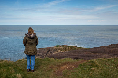 Rear view of man standing on shore against sea