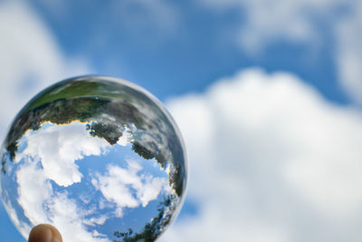 Upside down image of hand holding crystal ball against sky