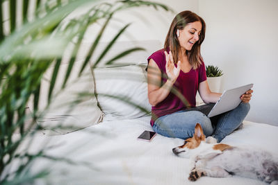 Woman with dog using digital tablet while sitting on bed