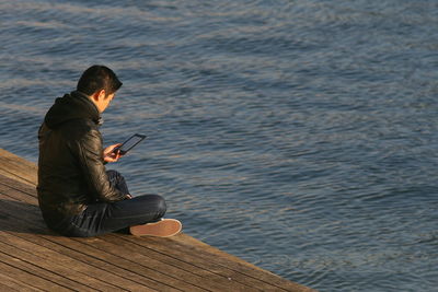 Rear view of man using phone on pier by river